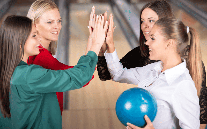 A group of women bowl in a modern bowling alley, surrounded by colorful lanes and bright, flashing lights